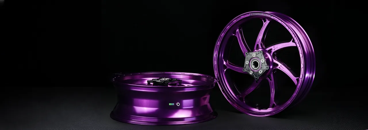 Pair of forged motorcycle wheels in a polished purple finish on a black studio floor